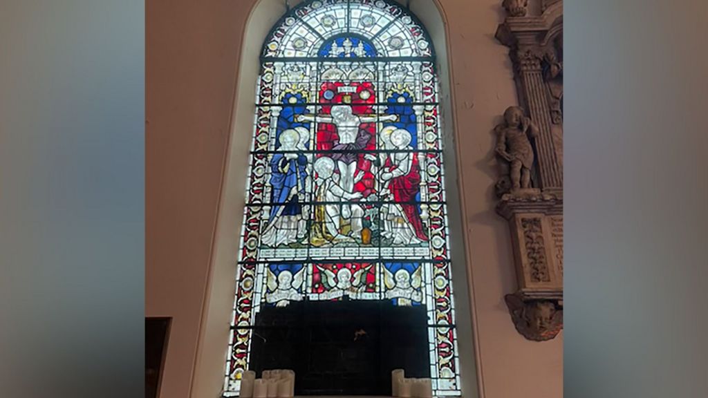 Black taped covers the bottom of a stained glass window which is blue red and yellow and depicts a scene which shows people surrounding the son of God
