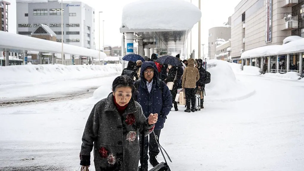 Japanese pedestrians walk near a bus stop in snowy conditions