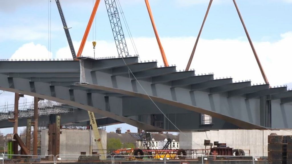 Aerial footage shows steelwork for a new viaduct arriving by barge and being installed.