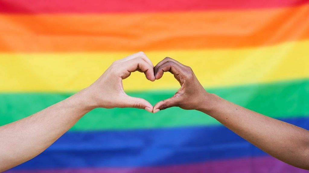 two hands making a heart in front of a pride flag
