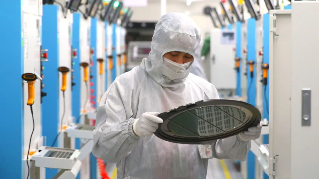 A worker in a white protective suit inspects a silicon wafer - a round disc.