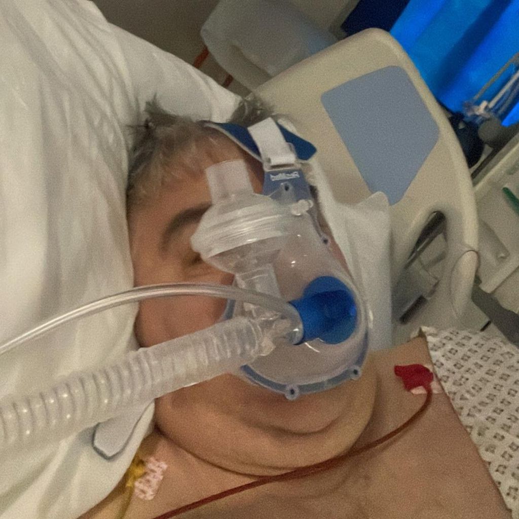 Stuart Brown on a hospital bed, unconscious with a respirator on his face