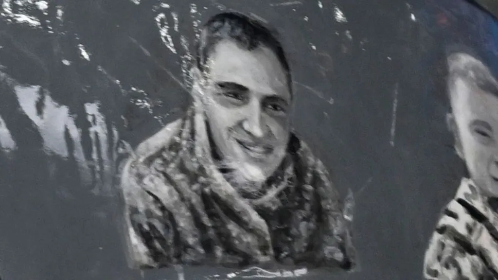 Close up of a black and white illustration of Andriy Yaremenko on the helmet. He has short, dark hair and is smiling.