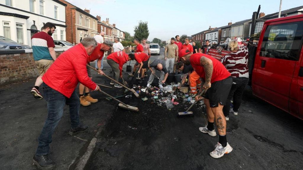 Residents in Southport cleaning up the debris after rioting. A group of men and women sweep burnt rubbish on a road