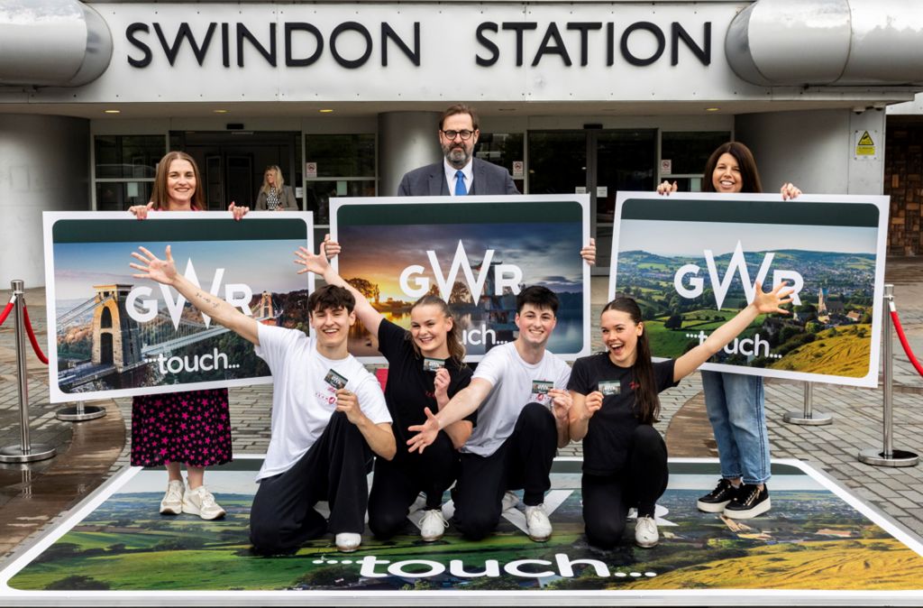 The four dancers, as well as three other representatives from Great Western Railway, stand outside Swindon Station holding three oversized GWR touch cards. 