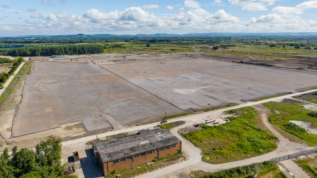 Aerial view of a large square plot of grey land surrounded by green vegetation