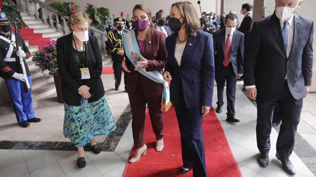 Honduran President Xiomara Castro in burgundy pant suit with blue and white sash, Kamala Harris in blue pant suit, red carpet, officials and security