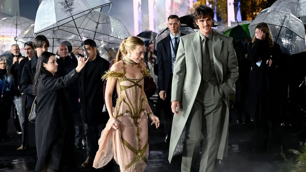Margot Robbie and Jacob Elordi in the rain at the Wuthering Heights premiere. People aroudn them are holding  umbrellas for them