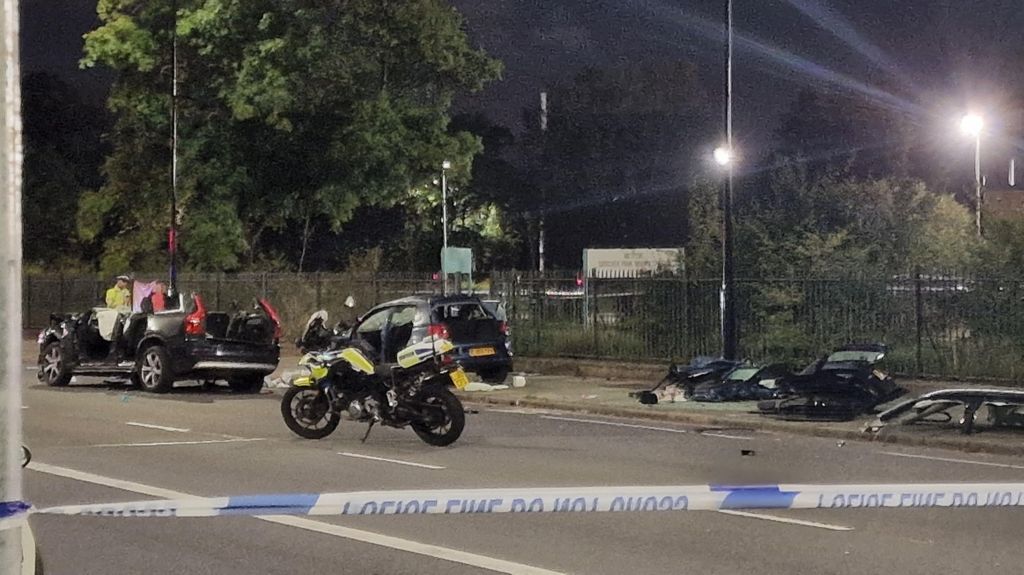 Car behind police tape with roof cut off. Police bike and officer can be seen along with debris