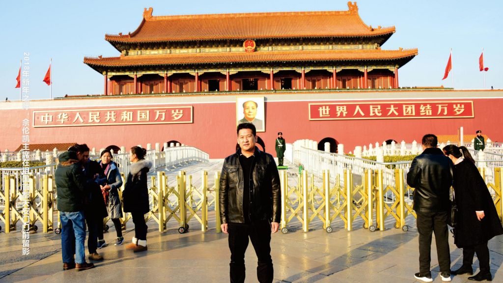 She Zhijiang wearing a black leather jacket and black trousers at Tiananmen Square, in front of yellow barricades