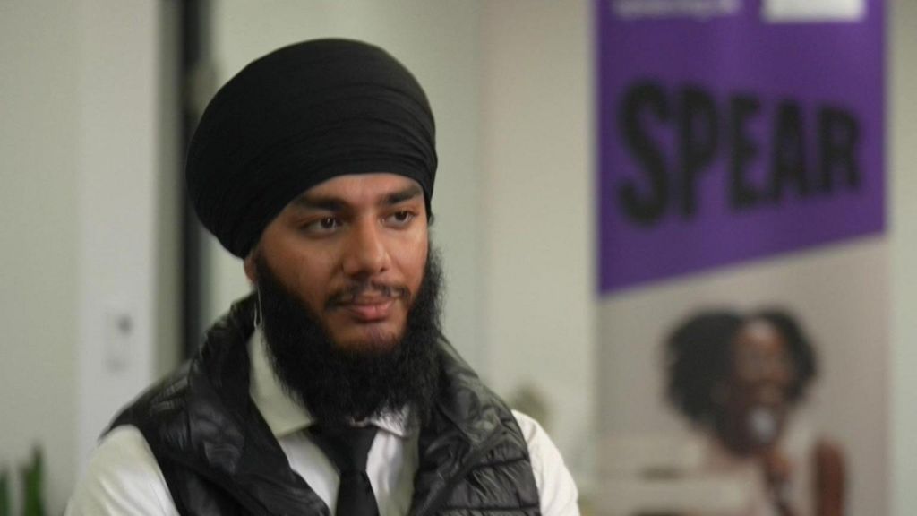 A young man in beard and turban looking serious. He is wearing a white shirt and tie