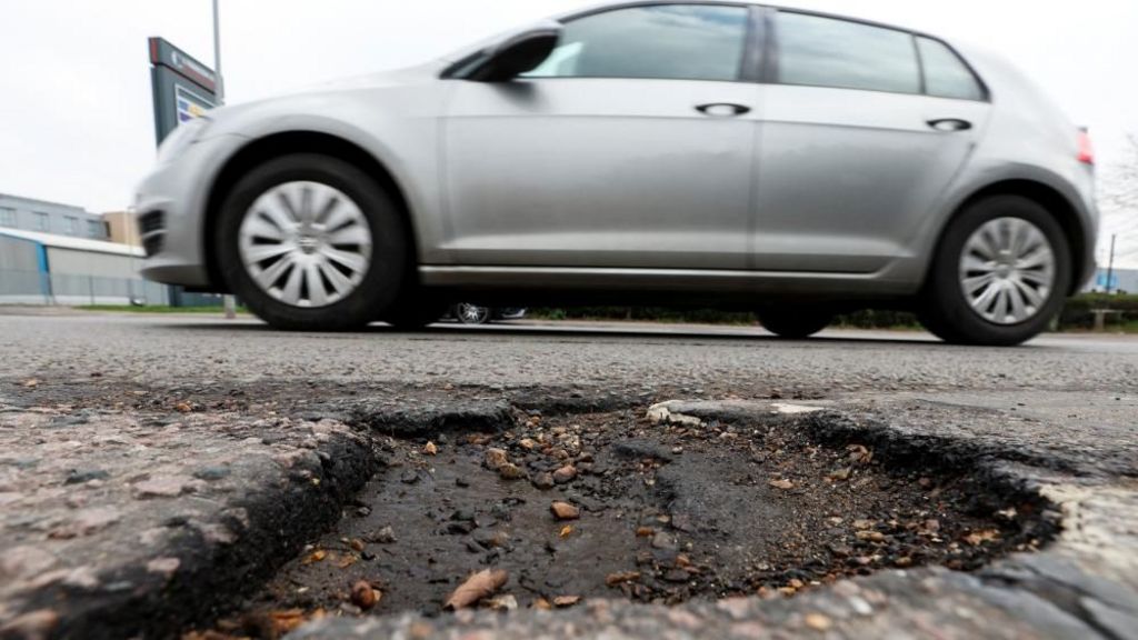 Grey car drives past pothole on a road