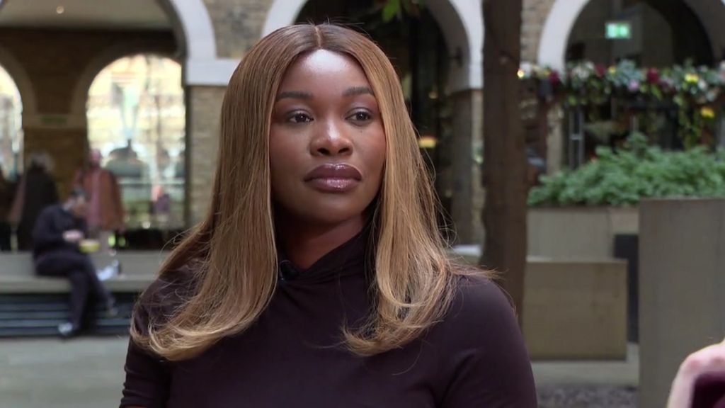 A woman with light brown hair and a black top looks slightly off camera, with the background blurred.