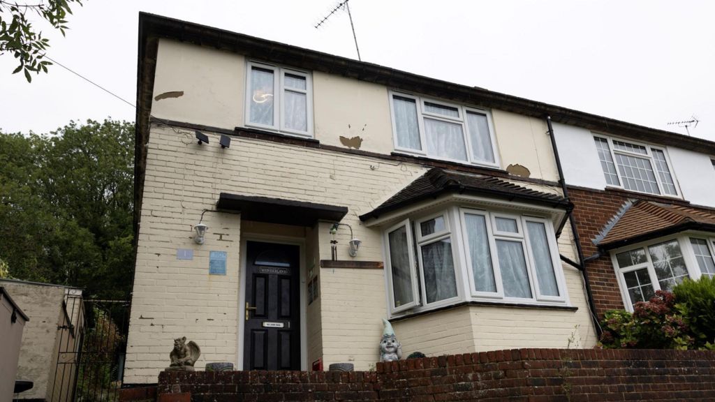 The exterior of a two-storey brick house painted in cream-coloured paint, viewed from the front.