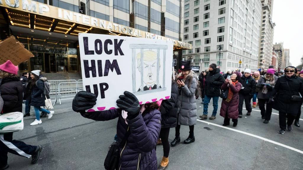 A marcher holds a sight that says "Lock Him Up!"with a picture of President Donald John Trump behind bars the Speaker of the United States House of Representatives who just submitted the articles of Impeachment for President Donald John Trump as she walks in front of Trump International Tower during the Woman's March in the borough of Manhattan in NY on January 18, 2020, USA