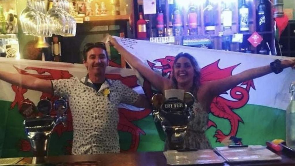 Workers holding the Welsh flag behind the bar