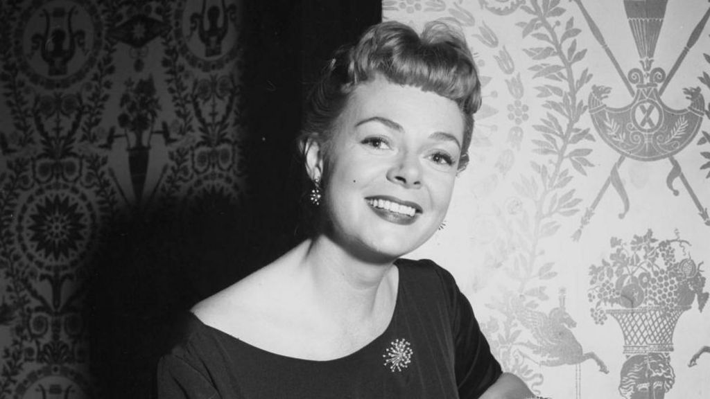 June Lockhart smiles in a black and white photo wearing a dress with short hair, earrings and a broach