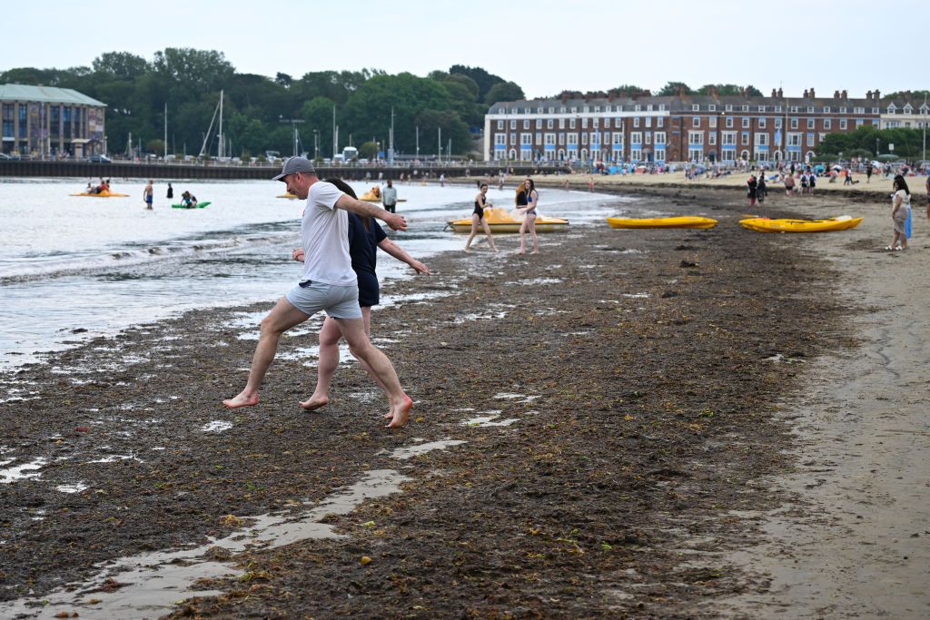 People jump over seaweed on Weymouth beach