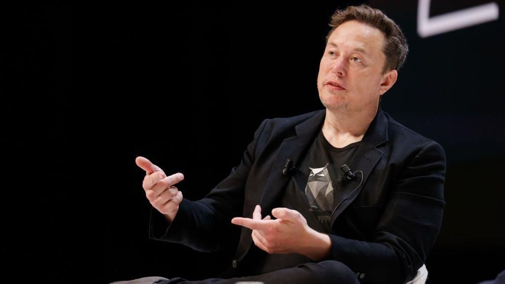 Elon Musk talking at a conference wearing a blue jacket