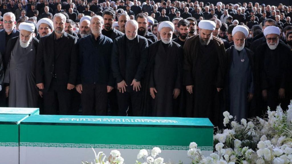 Iranian President Masoud Pezeshkian, Iran's Parliament speaker Mohammad Baqer Qalibaf and Chief Justice of Iran Gholam-hossein Mohseni Ejei with officials attend a prayer during a public farewell ceremony to pay their respects to late Supreme Leader Ayatollah Ali Khamenei. A large crowd can be seen in the background as everyone stands looking at the coffin