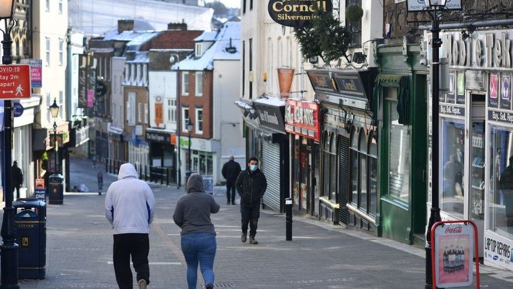 Pedestrians walk along a high street with the shops closed in Maidstone