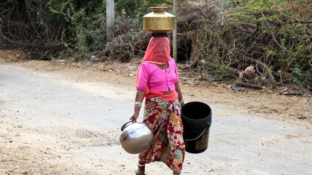 A woman carries buckets and containers to collect drinking water from a roadside water tap on the outskirts village of Ajmer in the Indian state of Rajasthan on 16 May 2019