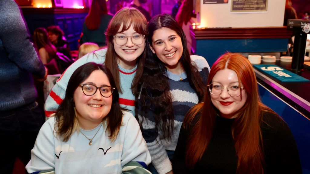 Alanna Charlton, Katie Curran, Madison Golan, and Bethan Smith. They are four young women smiling at the camera in a busy pub.