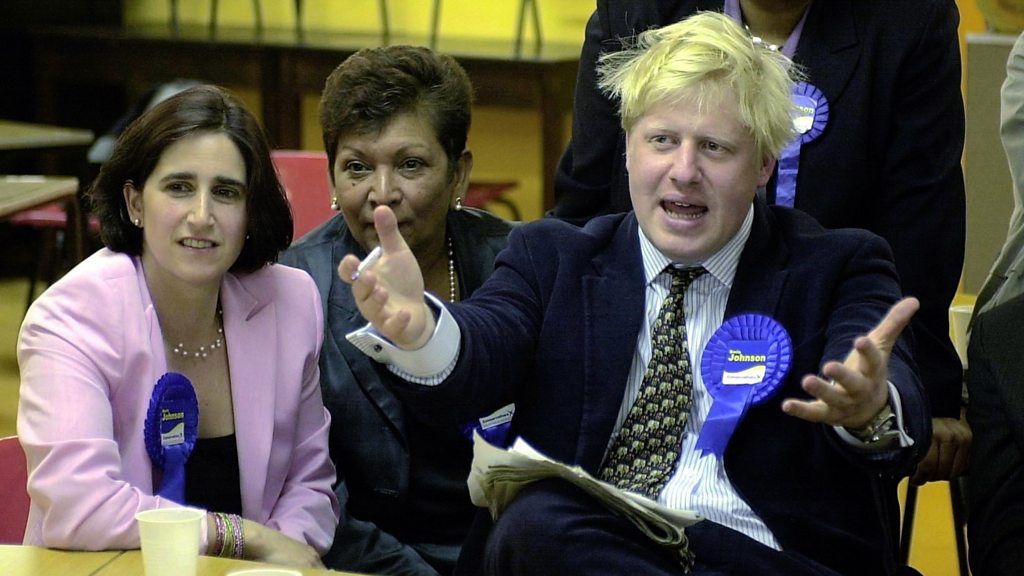 A young Boris Johnson sitting in a chair with hands animated in front of him