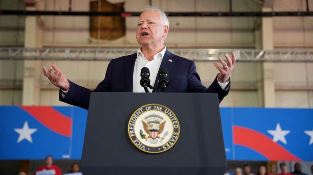 A man with white hair standing behind a podium that reads Vice President of the United States. There is a red white and blue background