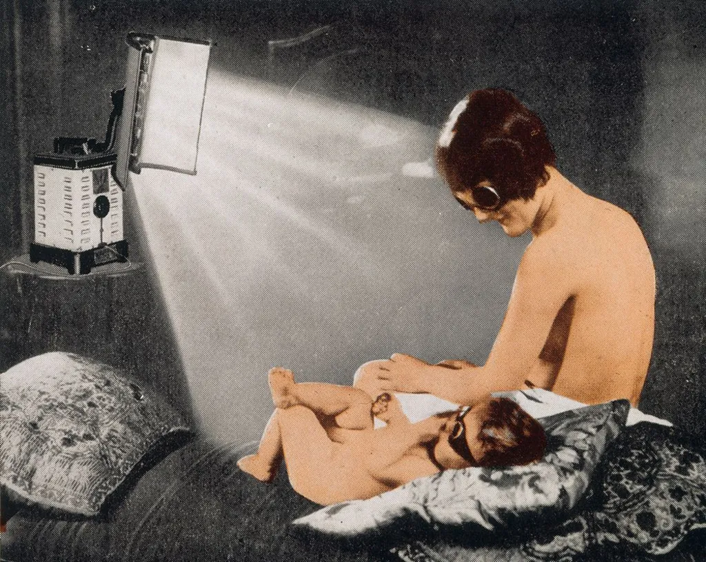 An archive advert from 1939, showing a woman and young child sitting on a bed in front of a heat lamp. They are depicted in colour and the background is in black and white. The woman is seen from the back, looking down at the toddler, who is lying with their right leg crossed over their left. They are both wearing goggles and are otherwise undressed but partially obscured.