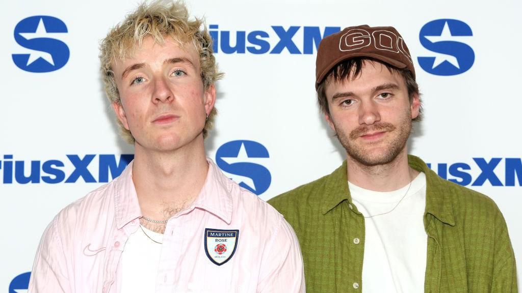 The two band members of Good Neighbours. Oli has short blonde hair and Scott has short brown hair. 