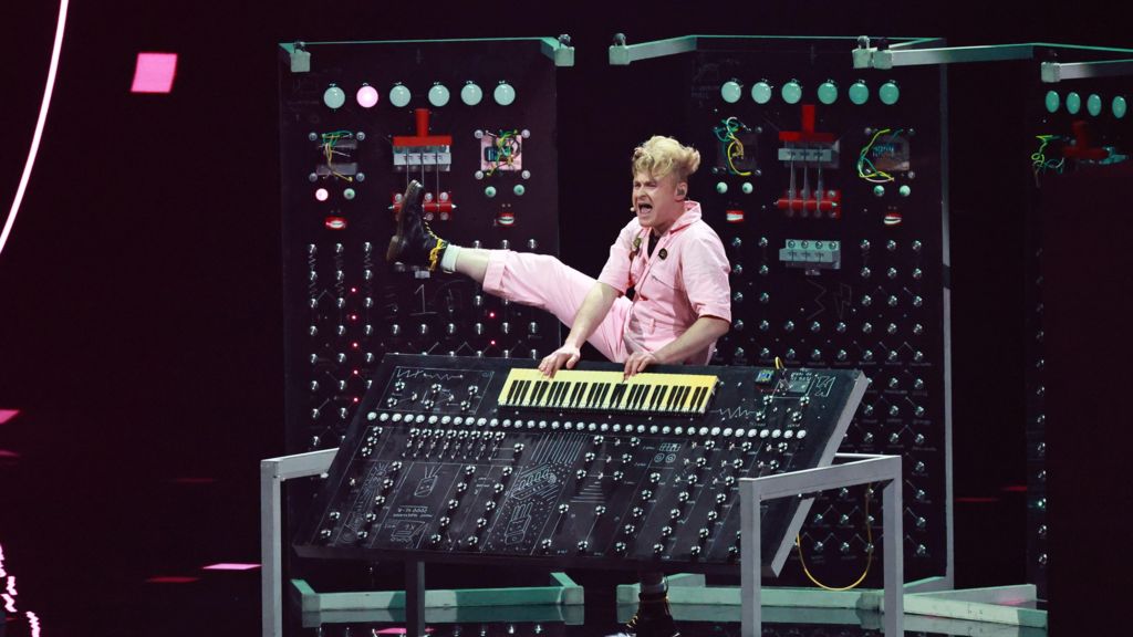 Sam Battle kicks his right leg into the air while playing a keyboard.