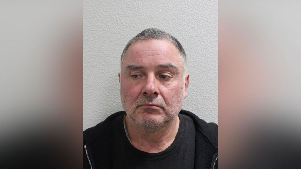 Custody image of Thomas McKenna, wearing a dark top, photographed against a plain wall.