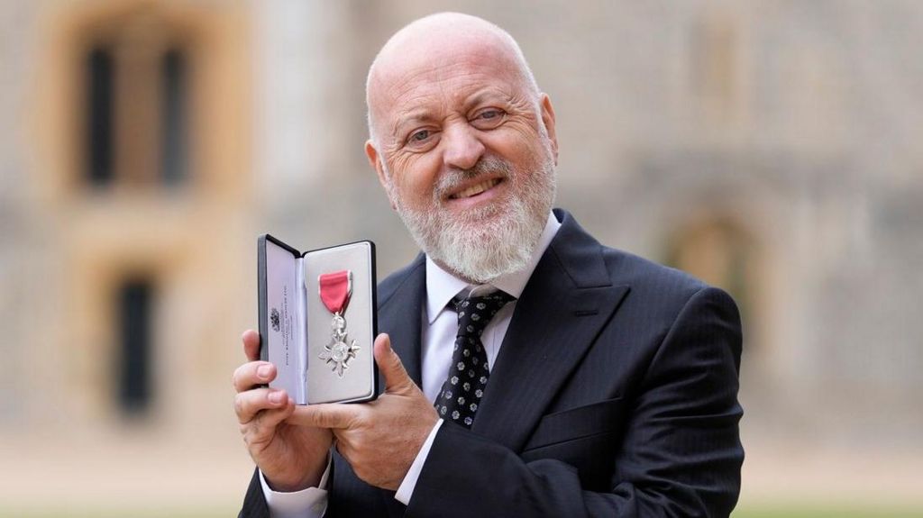 A close up picture of Bill Bailey holding up his MBE