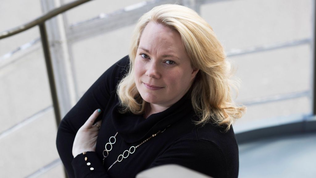 Blonde woman with her arms folded looking up at the camera