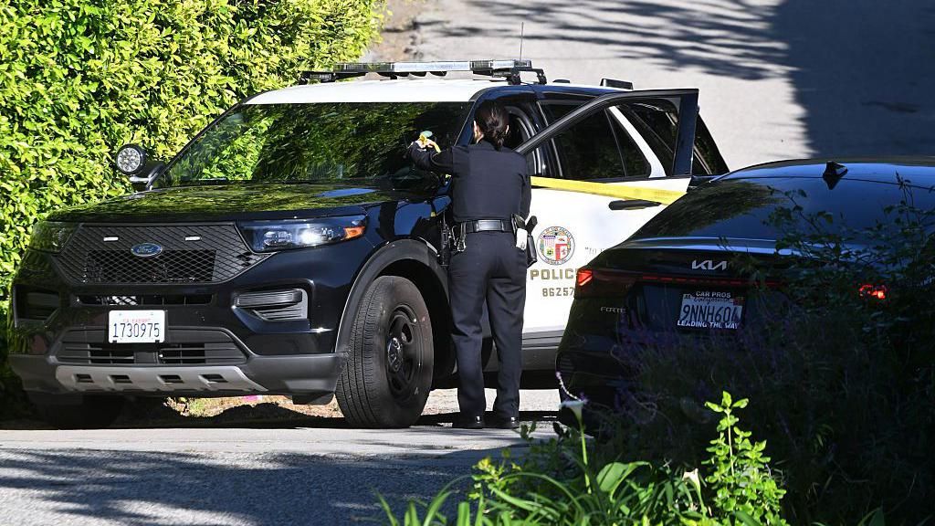 A police vehicle is parked on a road with an officer standing next to it