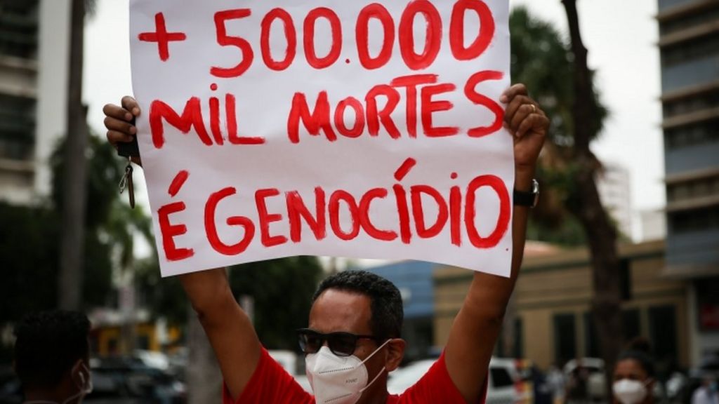 Manifestante segura cartaz escrito Mais de 500 mil mortes é genocídio durante protesto em junho de 2021 contra a atuação do governo Bolsonaro na pandemia de covid-19