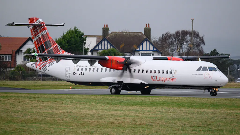 Loganair flight on the Ronaldsway runway. It's a small, white, propeller airplane with a tartan design on its tail fin.