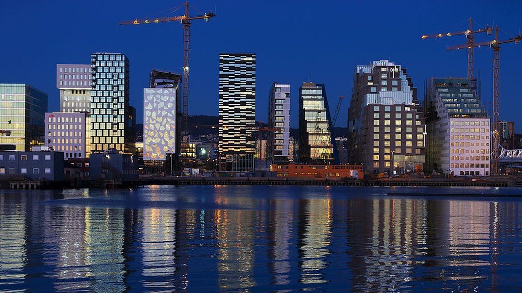 Buildings of The Barcode Project are reflected on the water at sunset in Oslo