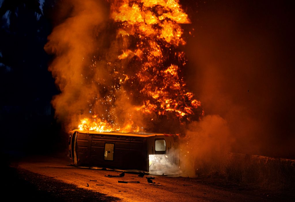 A coach on its side on fire, with huge flames rising into the night sky, in a scene from Corriedale