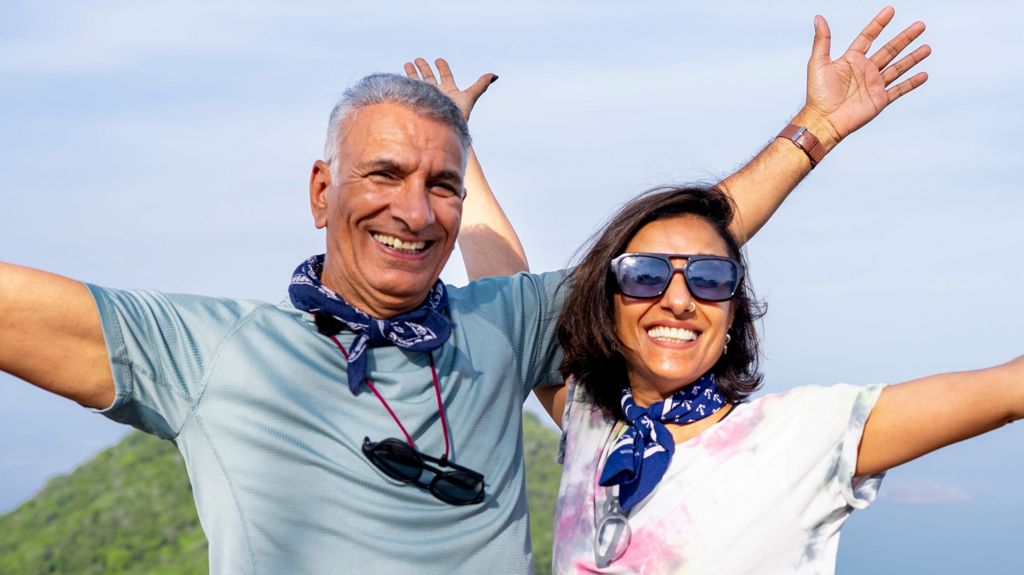 Anita Rani and her dad Bal standing together on a mountain, smiling and with their arms outstretched