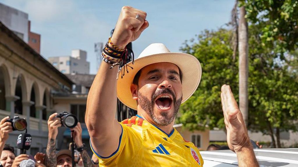 Abelardo de la Espriella cheers, wearing a hat and football shirt.