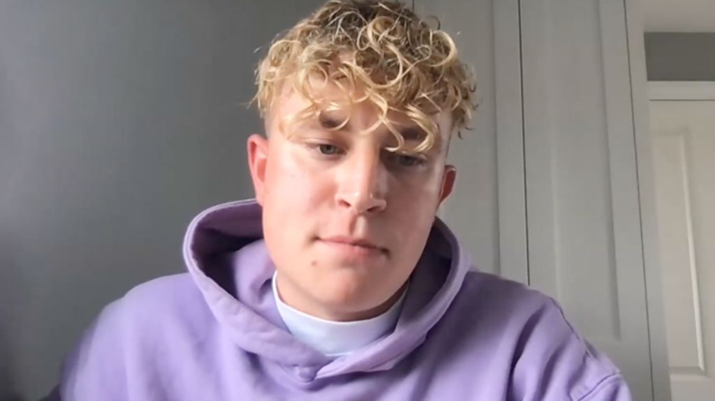 Lewis Rollins has dyed blonde hair and a purple jumper on.