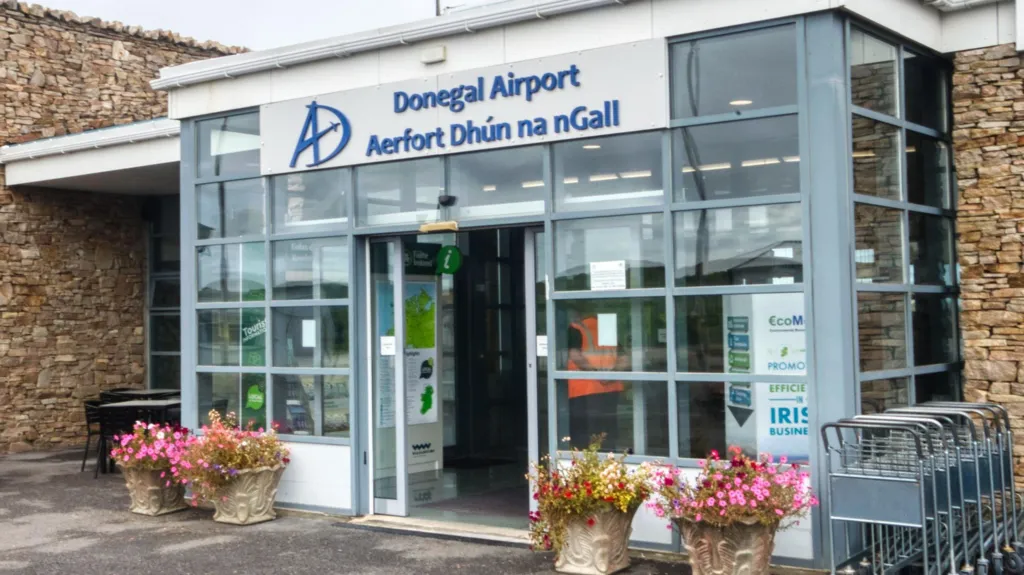 The front of Donegal airport, it is a small building with a glass entrance porch and stone walls on either side. The sign on the porch reads 