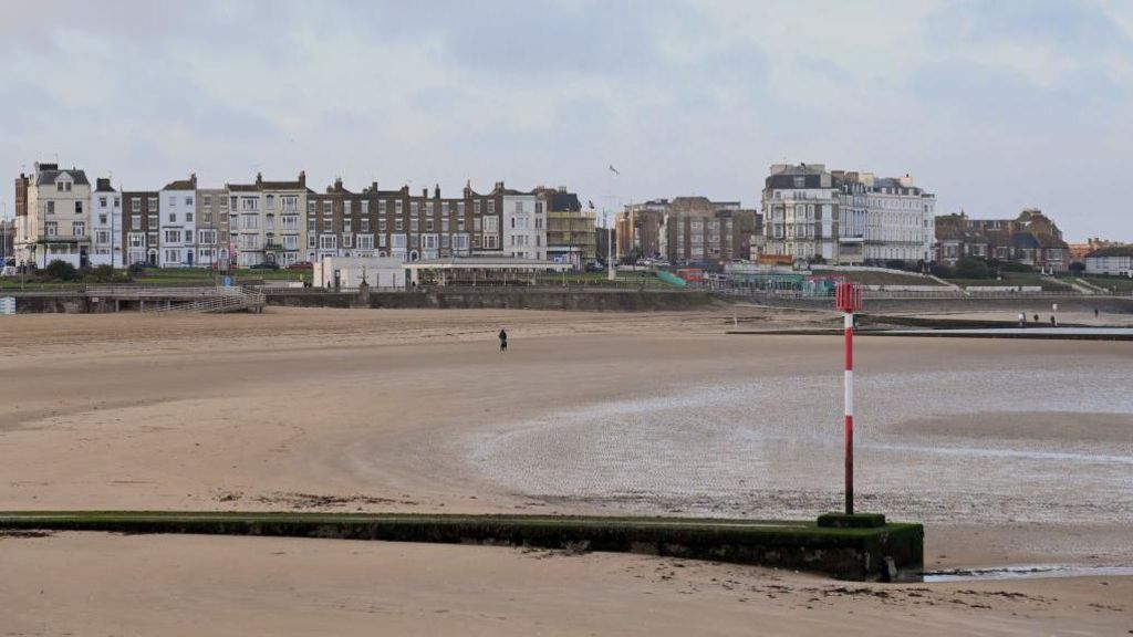 A picture of Margate Beach with one person standing on it. You can see the buildings on the promenade in the background.