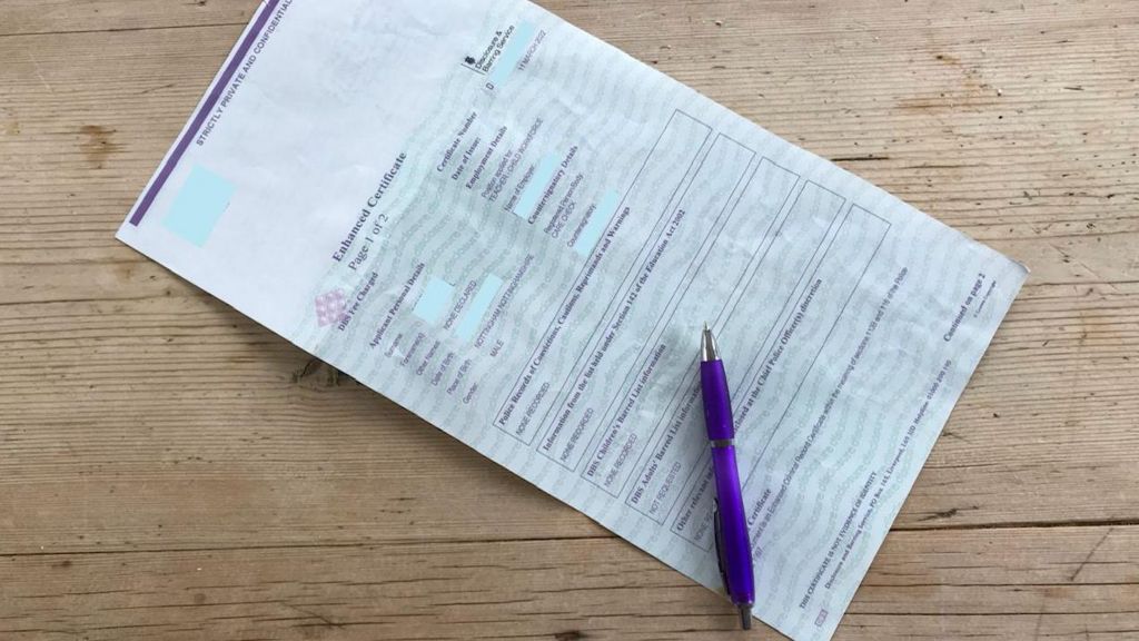 A redacted enhanced DBS check form on a table, with a purple pen placed on top