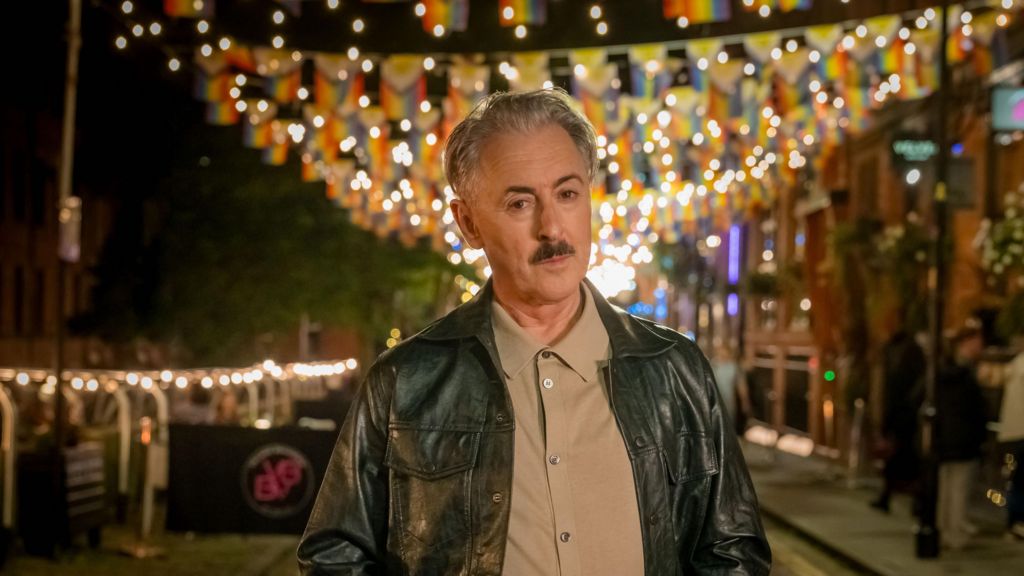 Alan Cumming dressed in shirt and leather jacket looking at the camera