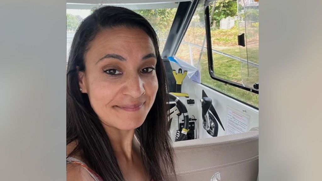 Syreeta Sandhu smiles at the camera. She is in the driver's seat of a car