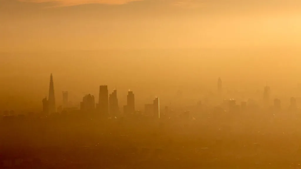 A yellow washed picture that is incredibly hazy, but you can see the outlines of buildings that make up the London skyline