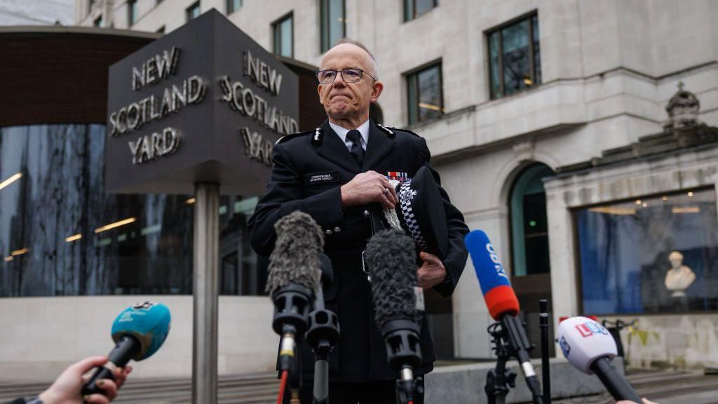 Sir Mark Rowley stands in front of a bank of microphones outside New Scotland Yard. He is in police uniform.